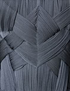 this is a closeup shot of a piece of grey pleated fabric. the fabric is folded and pleated in a intricate pattern, creating a complex and abstract design. the fabric is smooth and silky, with a slight sheen. the pleats are uniform and tight, creating a dense texture. the image is highquality, with sharp details and good lighting.
