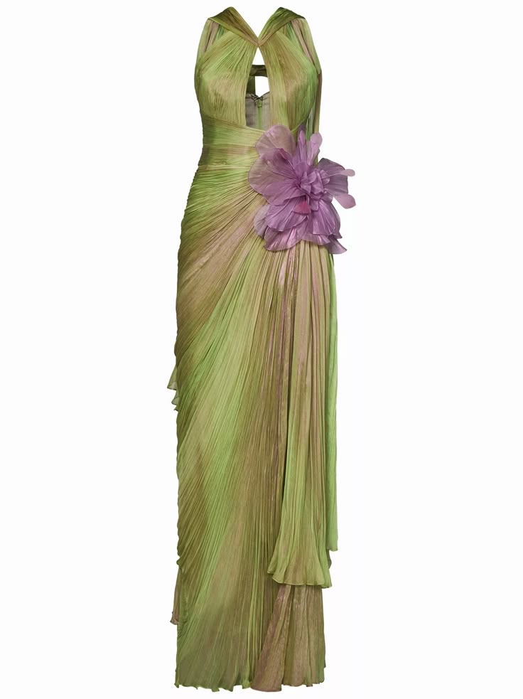an image shows a long, flowing green and purple gown with a large floral embellishment. the dress features a halter neckline with a small cutout at the bust. the fabric of the dress appears to be pleated and draped, giving it a textured look. a large, purple flower is attached to the dress at the waist. the gown is floorlength and gives off a sophisticated and elegant vibe.
