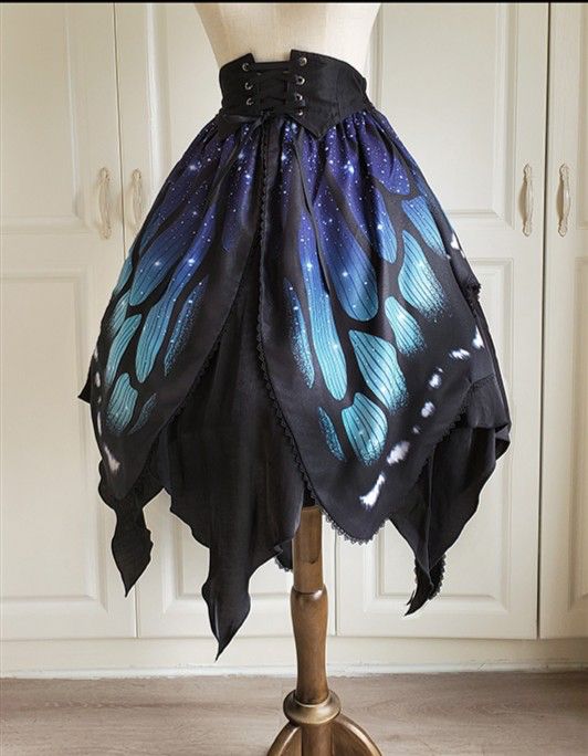 a black and blue butterfly wing skirt displayed on a mannequin. the skirt has a corsetstyle waistband and features a pattern of butterfly wings with stars on the upper portion. the bottom is shaped like butterfly wings with jagged edges. the skirt is presented against a background of white cabinets and a wooden floor.