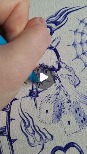 the image shows a closeup of a person's hand drawing an intricate design with a blue ballpoint pen. the drawing style is reminiscent of tattoo art and includes various elements such as dice, a chain, flames, thorns, a spiderweb, and a butterfly. the artist's hand is clearly visible, holding the pen and meticulously working on the details of the drawing. the drawing is rendered on a lightcolored paper surface. a play button overlay suggests the image is a still from a video demonstrating the creation process.