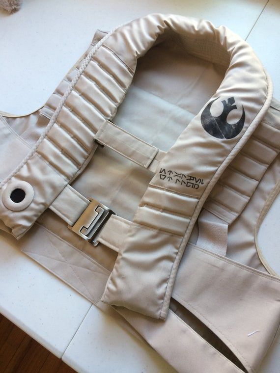 a close up image of a white vest with the rebel alliance logo and lettering. the vest is made of a thick fabric and has several buckles and straps. the vest appears to be a costume piece and is most likely for a star wars cosplay.