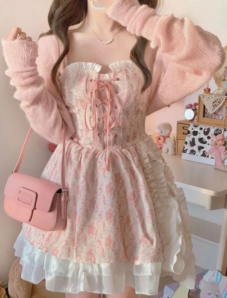 a young woman is wearing a pink floral dress with a laceup bodice and ruffled skirt. she has a pink cardigan sweater over her shoulders and a matching pink handbag. she is also wearing a necklace. the overall aesthetic is soft, kawaii, and feminine.