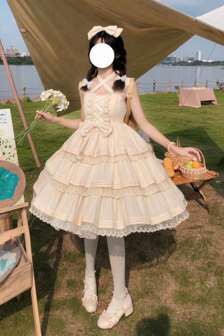 a woman wearing a flowing cream lolita fashion dress stands on a grassy riverbank.  she holds a bouquet of flowers in one hand and has a picnic basket with fruit and bread behind her. an easel with a partially painted canvas is visible to her left. she's positioned in front of a beige canvas tent.