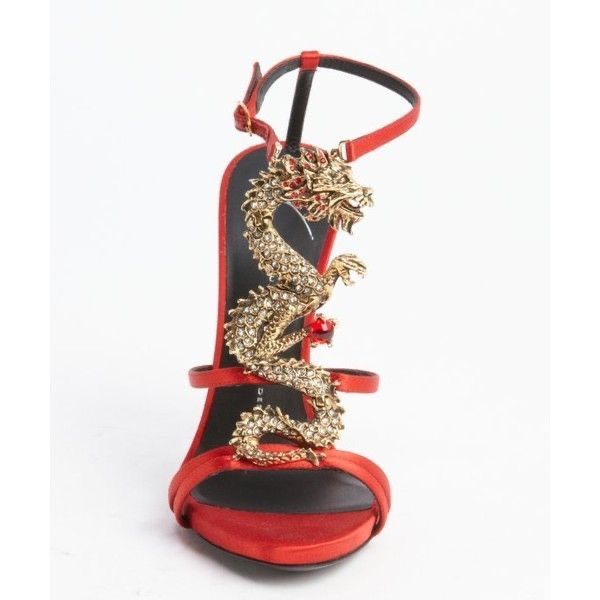 a closeup shot showcases a pair of elegant red satin high heels.  the most striking feature is a gold, jeweled dragon embellishment that wraps around the ankle strap and heel. the dragon is intricately detailed and appears to be made of gold metal with crystals or rhinestones. the shoes are poised on a clean white background, highlighting their luxurious design and craftsmanship.