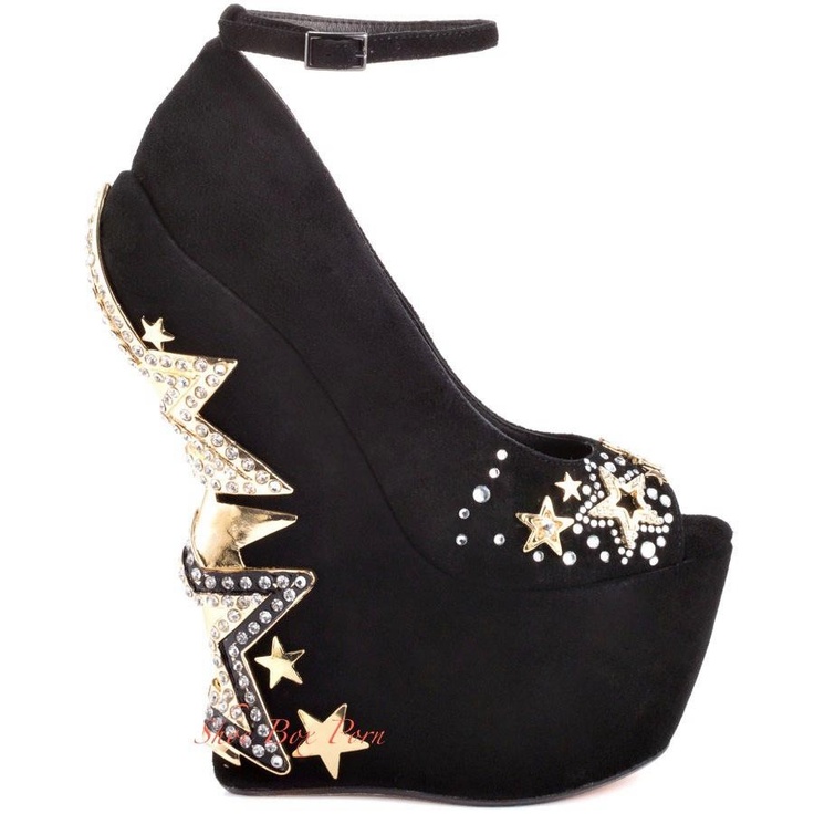 a black platform wedge shoe is displayed on a white background. the heel of the shoe has a lightning bolt design in gold with embedded rhinestones. there are gold stars and rhinestones scattered throughout the shoe. the shoe also has an ankle strap and a peep toe.