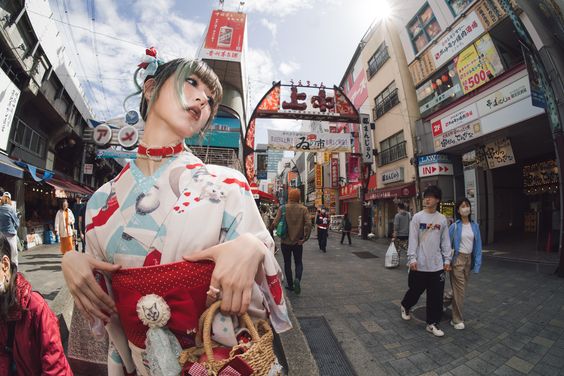 a young woman, dressed in a modern kimono, stands on a bustling city street in japan. the image is taken with a fisheye lens, creating a wideangle perspective that captures the energy and vibrancy of the urban environment. the woman is stylishly dressed, showcasing a blend of traditional and contemporary fashion. the street is crowded with people going about their day, and the surrounding buildings are adorned with colorful signs and advertisements. the sunny day provides natural lighting, illuminating the scene and highlighting the woman's outfit.