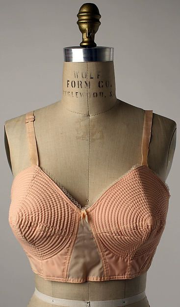 a peachcolored vintage bra is displayed on a mannequin. the bra has a unique circular stitched pattern on the cups and delicate lace trim. the mannequin is marked with "wolf form co."