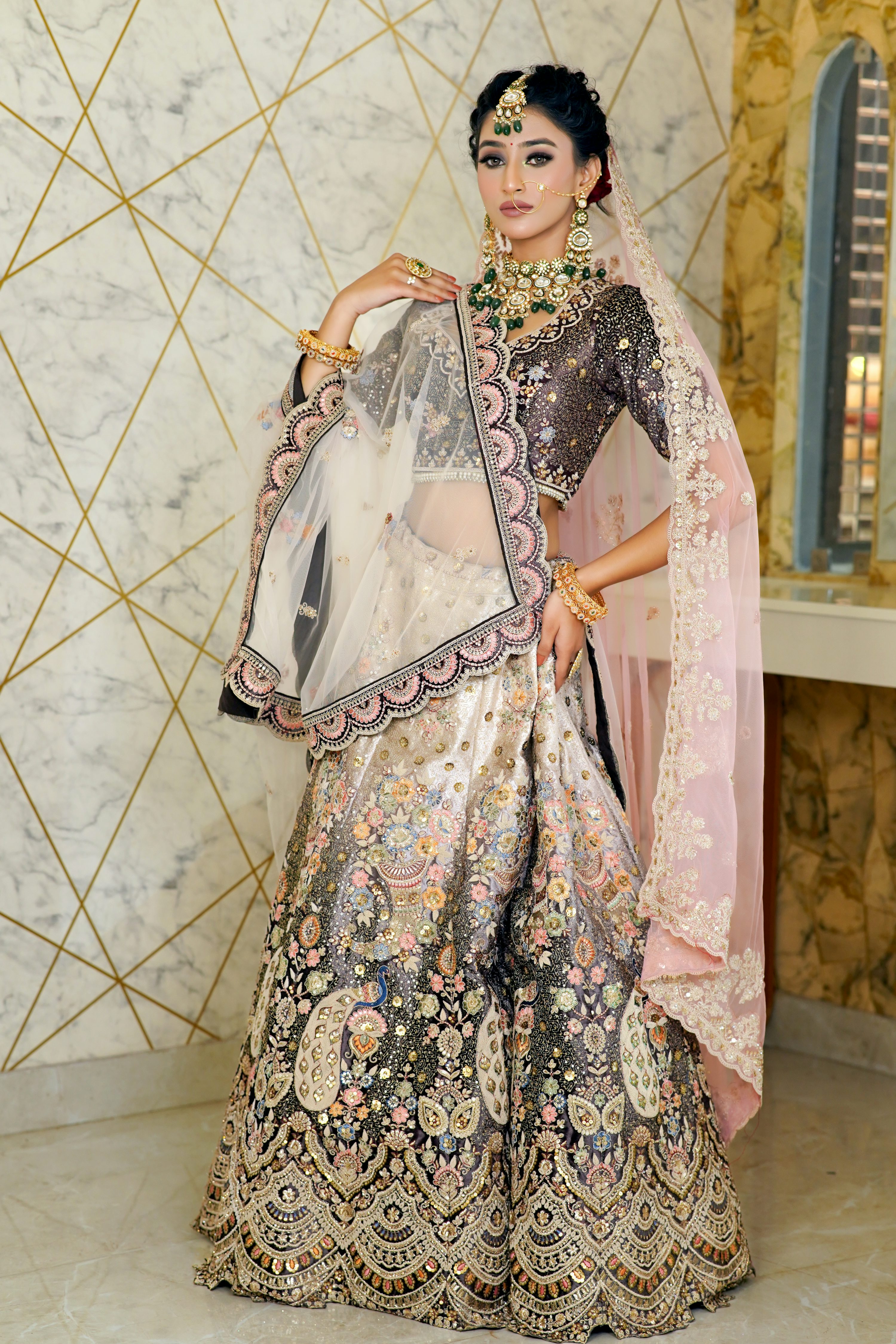 a stunning indian bride poses elegantly in a richly embroidered dark and lightcolored lehenga choli, adorned with intricate details and gold jewelry. the outfit features a combination of dark and light shades, a long, embellished dupatta, and exquisite traditional jewelry. the bride's makeup and hair are perfectly styled, and she holds her dupatta gracefully. the background showcases a textured wall with a geometric design. the overall image conveys a sense of luxury, tradition, and beauty.