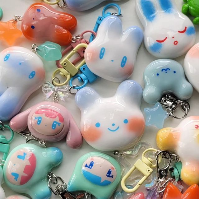 a closeup shot showcasing a collection of handmade resin keychains. the keychains are glossy and feature various cute and kawaii designs, including cartoon characters like cinnamoroll and my melody from sanrio, as well as bunnies and an octopus. they are made in pastel colors and have different types of clasps and accessories like stars and bows.