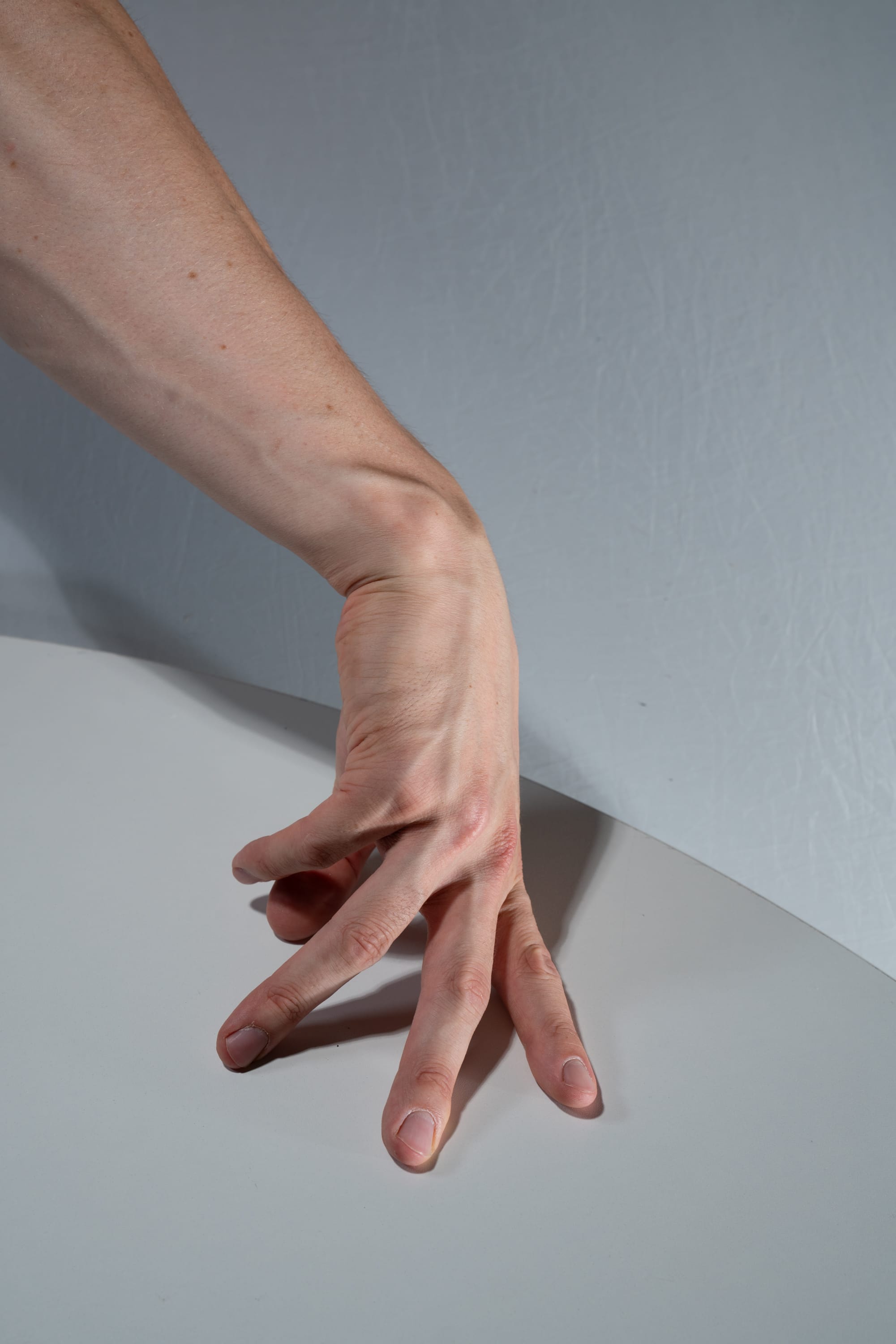 the image shows a caucasian male hand with its fingers splayed out on a white table. the light source is from the top left, casting a shadow to the right of the hand.