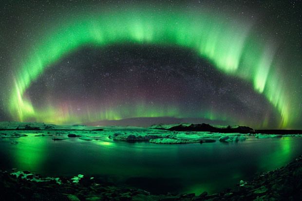 a breathtaking view of the aurora borealis, or northern lights, dancing across the night sky over a frozen lake in iceland. the vibrant green hues of the aurora are reflected in the still waters, creating a magical and otherworldly scene. the milky way can be seen in the background, adding to the celestial spectacle. the landscape is covered in a blanket of snow, creating a winter wonderland.