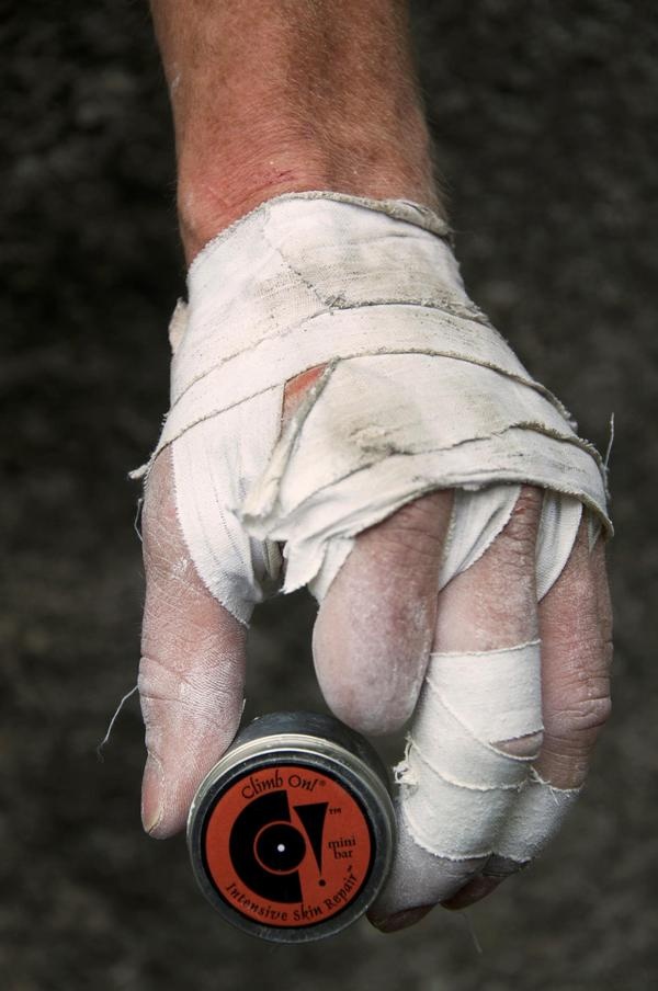 a hand with a white bandage is holding a small tin of "climb on!" mini bar intensive skin repair cream. the hand is likely that of a rock climber, as the cream is designed for climbers to repair their skin.