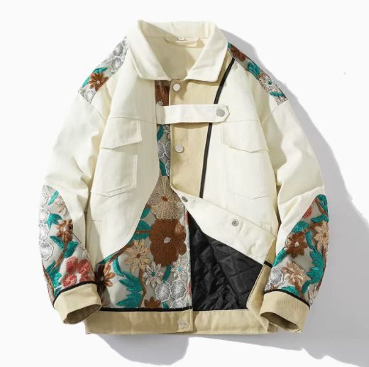 a white denim jacket with floral embroidery on the sleeves and back. the jacket has a patchwork design with beige and black panels. the jacket is a casual and stylish piece that would be perfect for spring or summer.