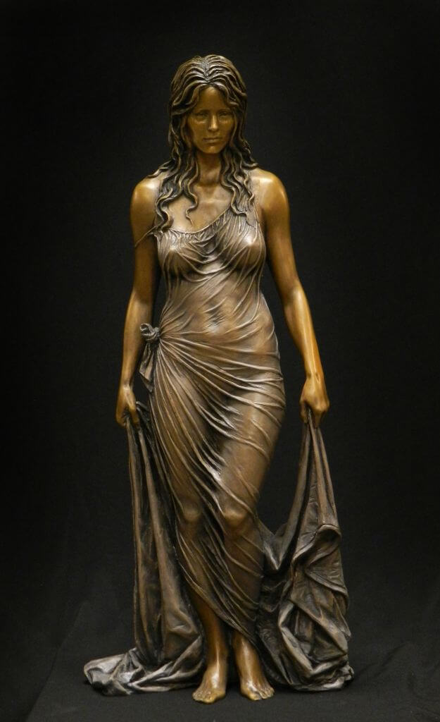 a bronze sculpture of a woman standing with a flowing gown draped around her body. the statue is illuminated with studio lighting against a black background.