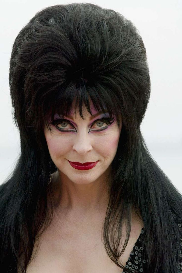 a woman with long black hair and dramatic makeup is wearing a black sequined dress. she is looking at the camera and her lips are painted a bright red. the background is white.