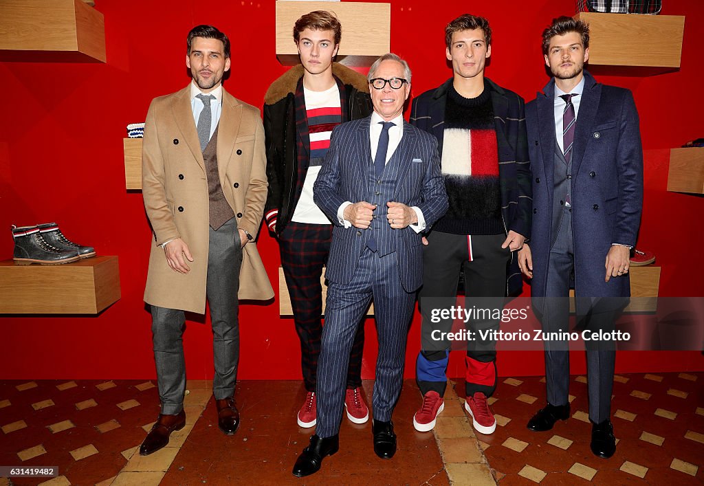 a group of five men posing in front of a red backdrop. the man in the center is tommy hilfiger, wearing a striped navy blue suit and glasses. the other men are wearing various outfits, including suits, coats, sweaters, and plaid pants. they are all dressed in men's fashion, and the getty images logo is visible in the bottom right corner.