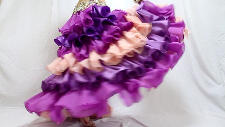 a belly dancer in midmotion, wearing a vibrant ruffled skirt in shades of purple and peach, the skirt is made of satin and the dancer is wearing a sequin belt.