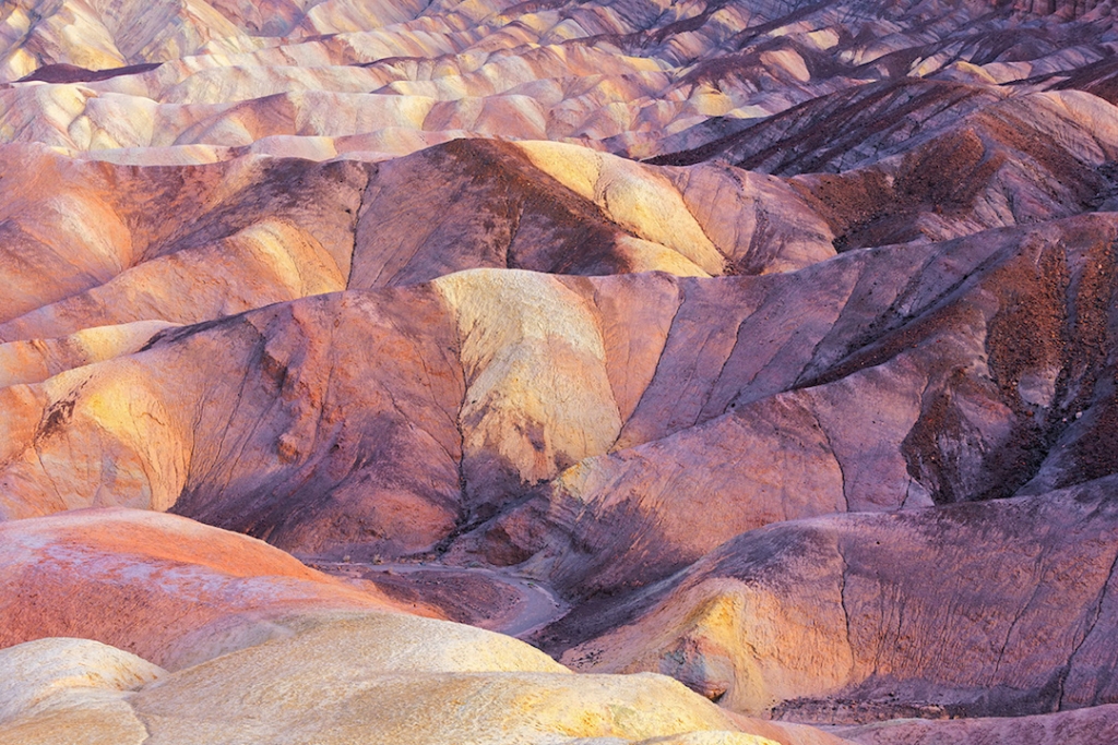the image is a scenic landscape of death valley national park in california. it features a series of colorful, eroded hills and ridges. the geologic formation displays striped patterns and earth tones. the arid environment and natural light contribute to the dramatic appearance of the badlands landscape.