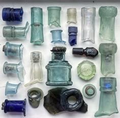 a collection of various vintage glass bottles, jars, and other glass objects arranged on a white surface.  the objects are of different shapes and sizes, and they are all made of clear or colored glass. the glass objects include clear bottles, blue bottles, green bottles, brown bottles, and a black bottle. the objects are arranged in a way that is both pleasing and interesting.  the image is welllit, and the objects are in focus. the background is white, which allows the objects to stand out.
