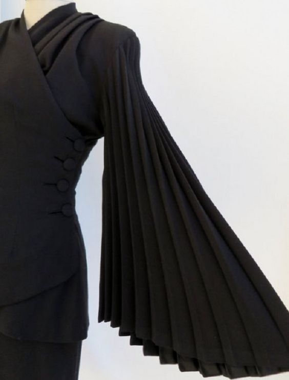 a black dress with long pleated sleeves is a timeless piece of clothing that can be dressed up or down. this particular dress has a fitted bodice and a flowing skirt, and the sleeves are pleated all the way from the shoulder to the wrist. the dress is perfect for a special occasion, or for adding a touch of elegance to a casual outfit.