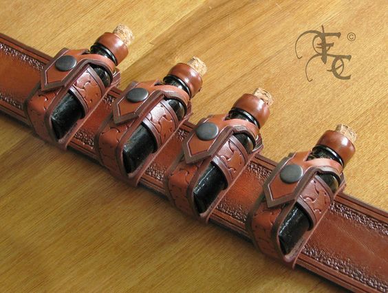a brown leather belt with four small glass bottles slotted into individual tooled leather holders. each bottle has a cork and is laying on its side. the belt is laying on a wooden surface.