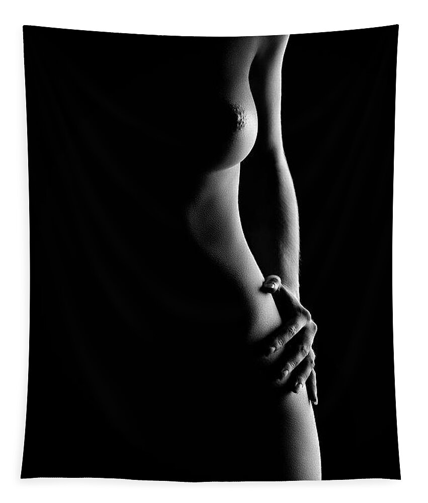 the image is a black and white, closeup shot of a nude woman's torso and hip.  the lighting is dramatic, using strong chiaroscuro to highlight the curves of her body while leaving much of the background and some areas of her body in deep shadow. the woman's hand rests gently on her hip. the overall mood is sensual and artistic, with a focus on the interplay of light and shadow to create a striking visual effect. the image is a study of form and light.