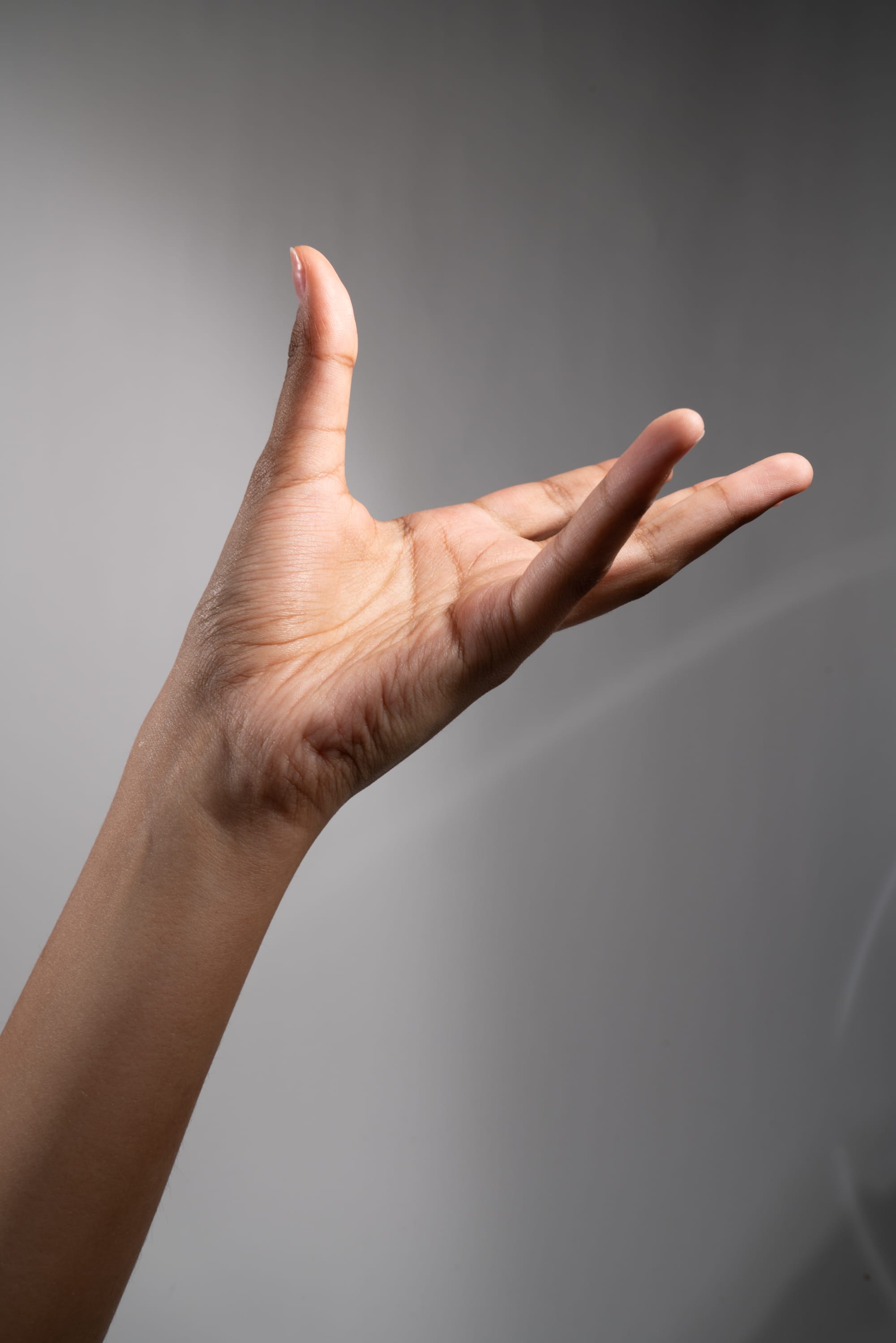 a hand is reaching out with an open palm, as if offering something or gesturing. the background is a neutral gray, suggesting a studio setting with deliberate lighting.