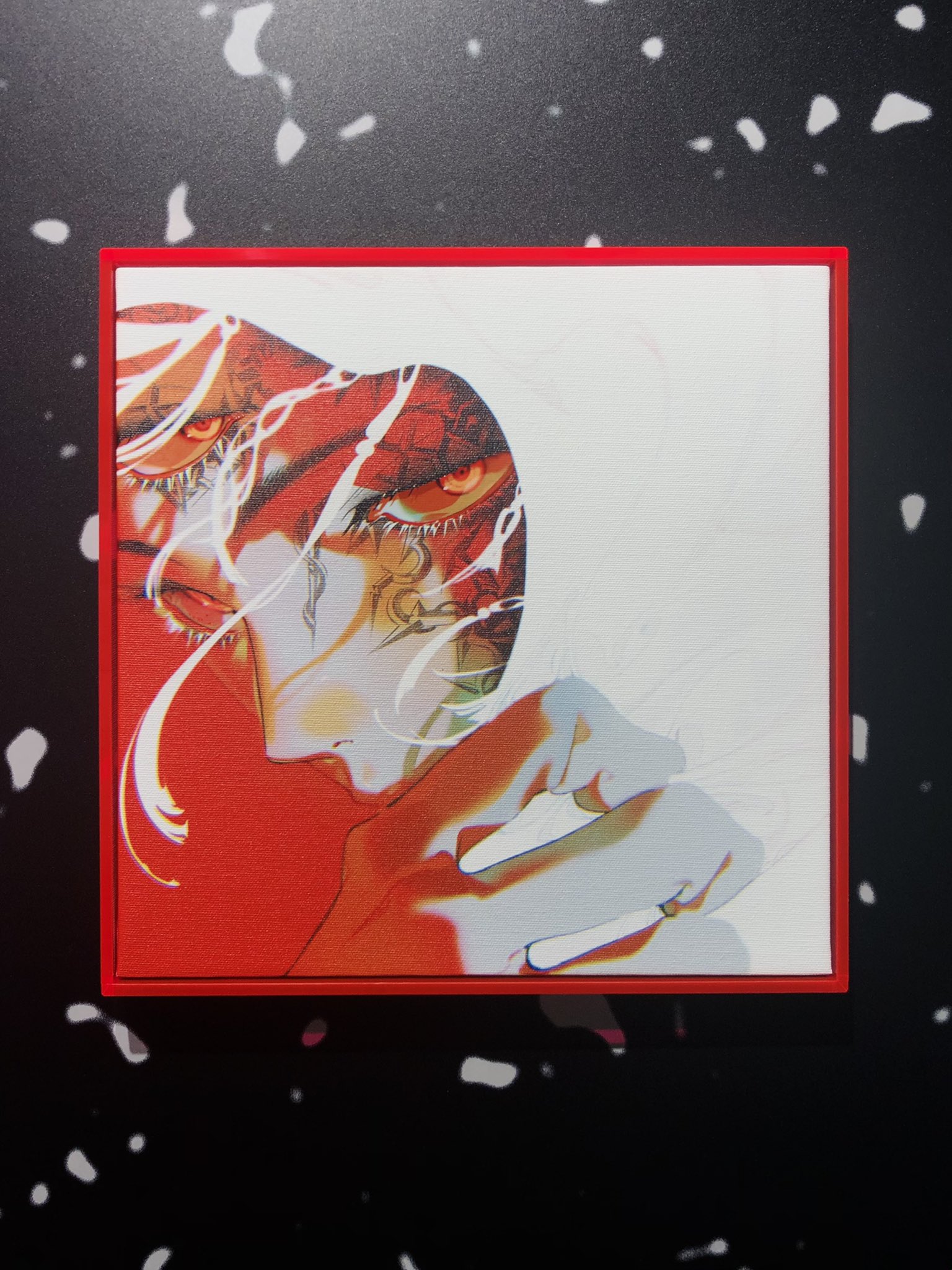 a framed illustration on a textured black and white wall. the illustration is primarily in shades of red, black, and white, and depicts a woman's face and hand in a stylized manner. her eyes are a striking red, drawing the viewer's attention.