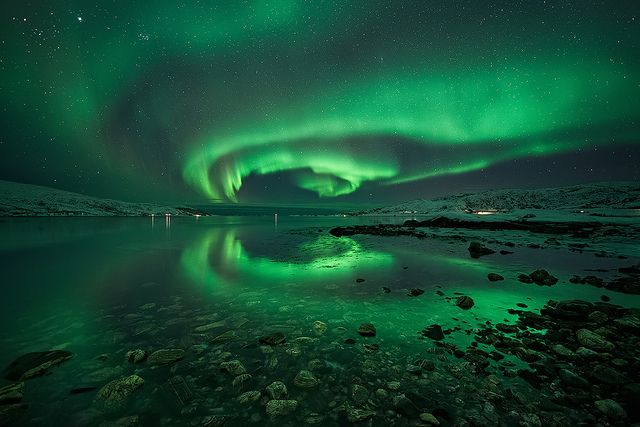 a breathtaking panoramic view of the aurora borealis, also known as the northern lights, dancing across the night sky. the vibrant green light illuminates the scene, creating a magical and surreal ambiance. the aurora's reflection in the calm water adds another layer of beauty to the image, creating a mirror effect of the celestial spectacle. the rugged coastline and scattered rocks provide a sense of scale and contrast against the celestial wonder. the composition captures the aweinspiring beauty of this natural phenomenon, inviting viewers to imagine themselves amidst this enchanting spectacle.