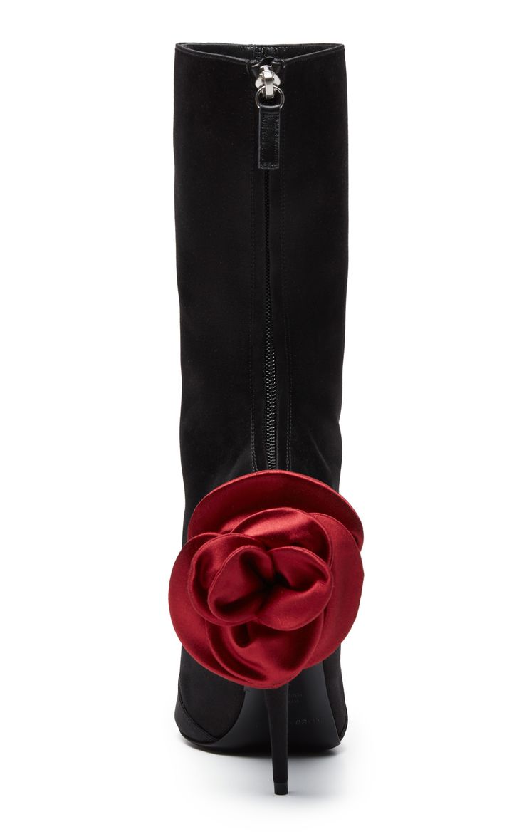 the image shows a pair of women's black suede high heel boots.  the boots are anklehigh and feature a prominent, large red satin rose embellishment on the back of one heel. a zipper is visible on the back of the boots for closure.  the image is a rear view, showcasing the boots in their entirety.  the overall style is elegant and stylish.