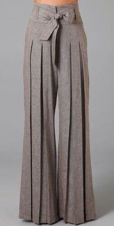 a woman is wearing a pair of widelegged, brown palazzo pants. the pants have a pleat design and a belt with a bow at the front.  they are a fashionable style that can be dressed up or down.