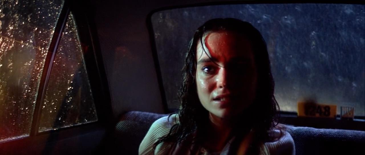 a scared looking woman sits in the backseat of a taxi, her face is wet and illuminated by a mysterious glow. the rain is coming down outside, making the window appear blurry and creating a sense of unease.