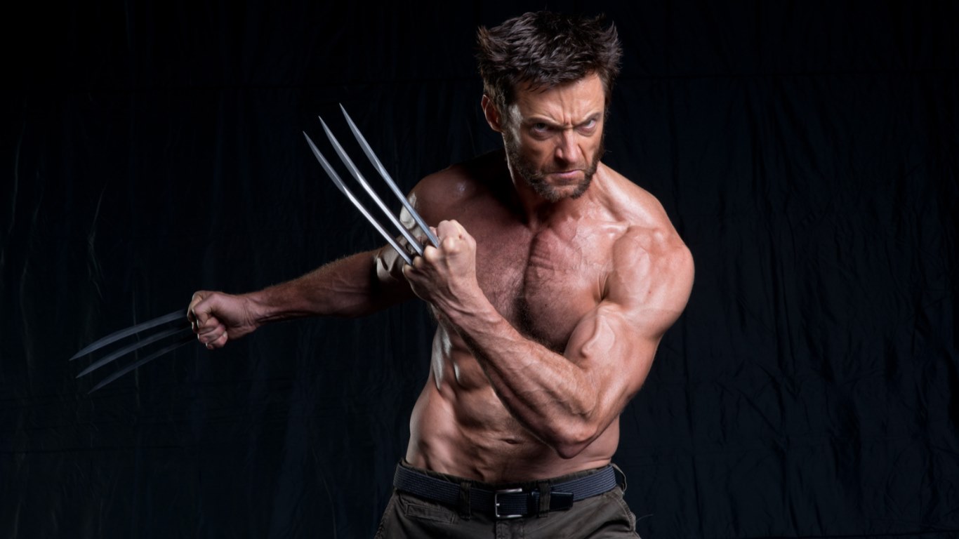 a portrait of a shirtless and muscular hugh jackman as wolverine, posing with his signature metal claws extended. he is looking forward with an angry expression on his face. the background is a dark, neutral tone.