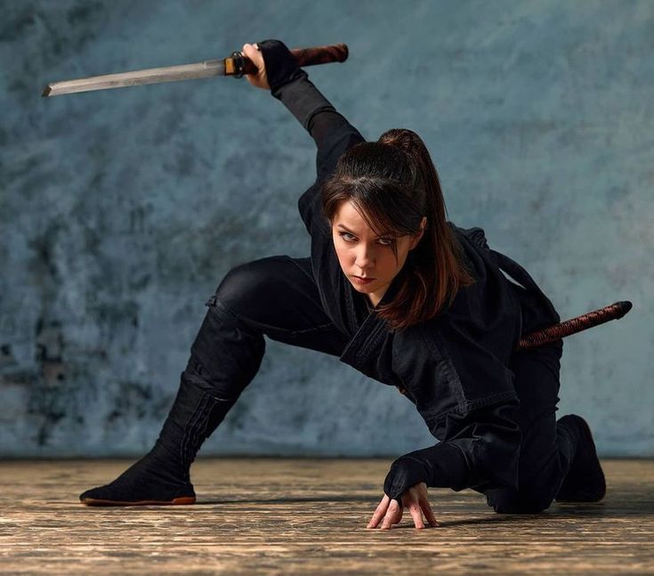 a woman dressed in black ninja attire, crouching low to the ground with a katana in hand,  demonstrating martial arts skills and readiness. the focus is on her intense gaze and the sharp blade, emphasizing her warrior spirit and the imminent threat posed by her.