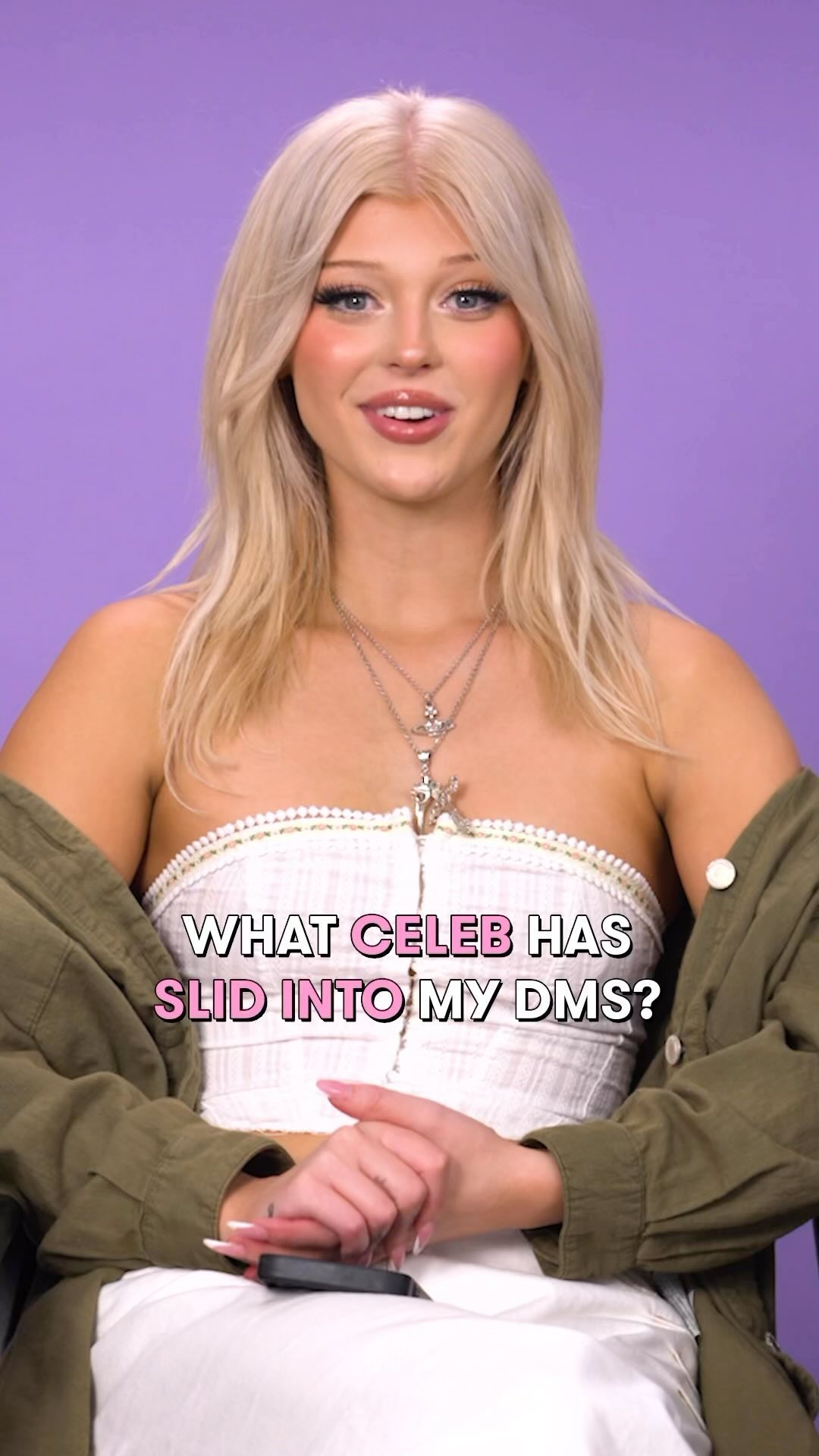 a blonde woman with long hair is sitting in front of a purple background, wearing a white top, green jacket, and silver necklaces. she is speaking to the camera and text overlay says "what celeb has slid into my dms?"