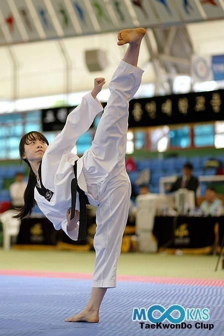a female taekwondo athlete performs a powerful kick during a training session or competition. she wears a white dobok (uniform) with a black belt and is focused on her technique. the image captures her determination and agility as she executes a dynamic move.