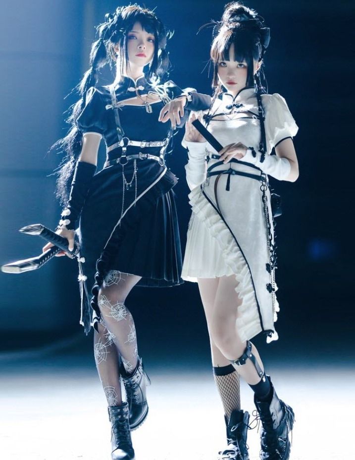 two young women dressed in anime cosplays pose for a photoshoot in a studio. the girl on the left wears a black dress with black and white accents, while the girl on the right wears a white dress with black and white accents. both girls are wearing black boots and have their hair styled in a similar manner. they are both looking at the camera. the image is welllit and shows the detail of their outfits.