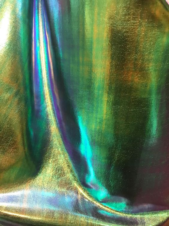a closeup shot of a holographic fabric in green, gold, and blue shades, with a diagonal fold, creating a shimmering and textured background.