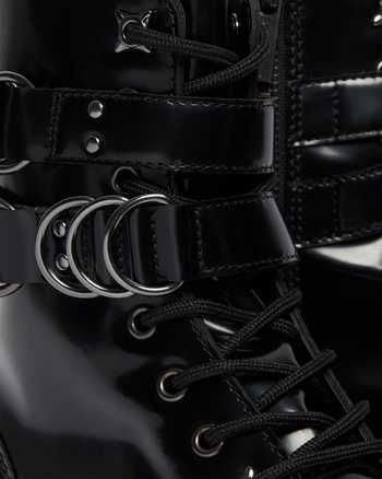 a closeup image shows black leather boots with buckles and laces. the boots have a shiny, patent leather appearance and feature multiple straps with metal rings. the laces are black and crisscross up the front of the boot.