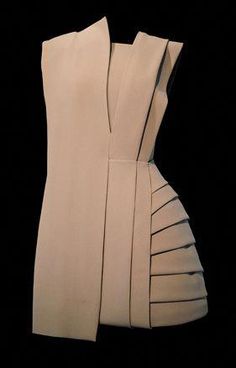 this is a closeup photo of a beige dress with pleated details. the dress is designed in a minimalist style with a simple silhouette that is both elegant and sophisticated. the dress is made of highquality fabric that gives it a luxurious feel and look. the pleated details add a touch of drama and movement to the dress. it is a perfect choice for a formal event or a night out.