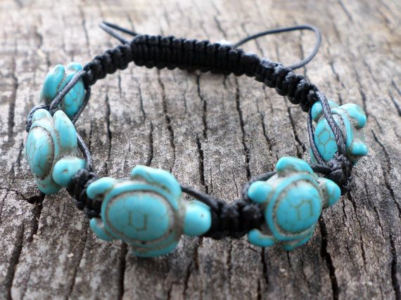 a closeup shot of a turquoise sea turtle bracelet on a wooden background. the bracelet is made of black cord and features several turquoise sea turtle charms.