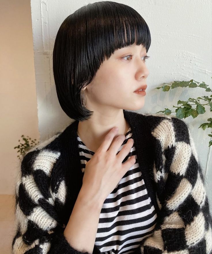 a young woman with black short bob hair and bangs looks to the side, wearing a white and black striped shirt under a black and white checkerboard sweater.