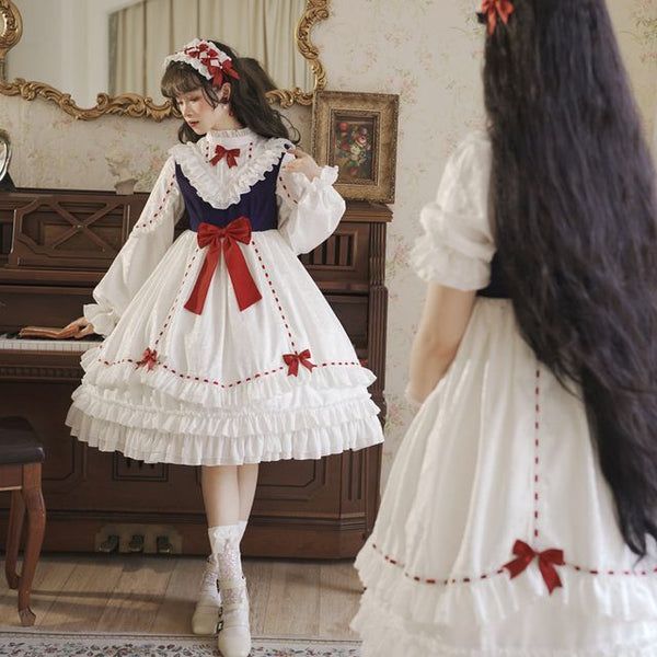 a young woman is posing in front of a mirror wearing a white and navy blue lolita fashion dress. the dress is adorned with red ribbons and lace. the woman has long black hair and is wearing a matching headband.  the image appears to be taken indoors in a welllit room.