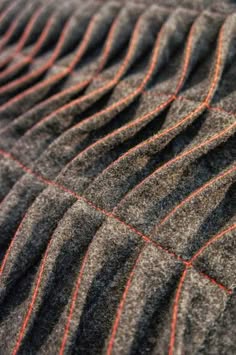 close up of a textured fabric with a pleated design, giving it an interesting pattern. the material is grey and brown in color and is made from woven threads.  the pleats are defined by a red stitch running along the folds.  the image highlights the intricate details and the rough texture of the fabric.