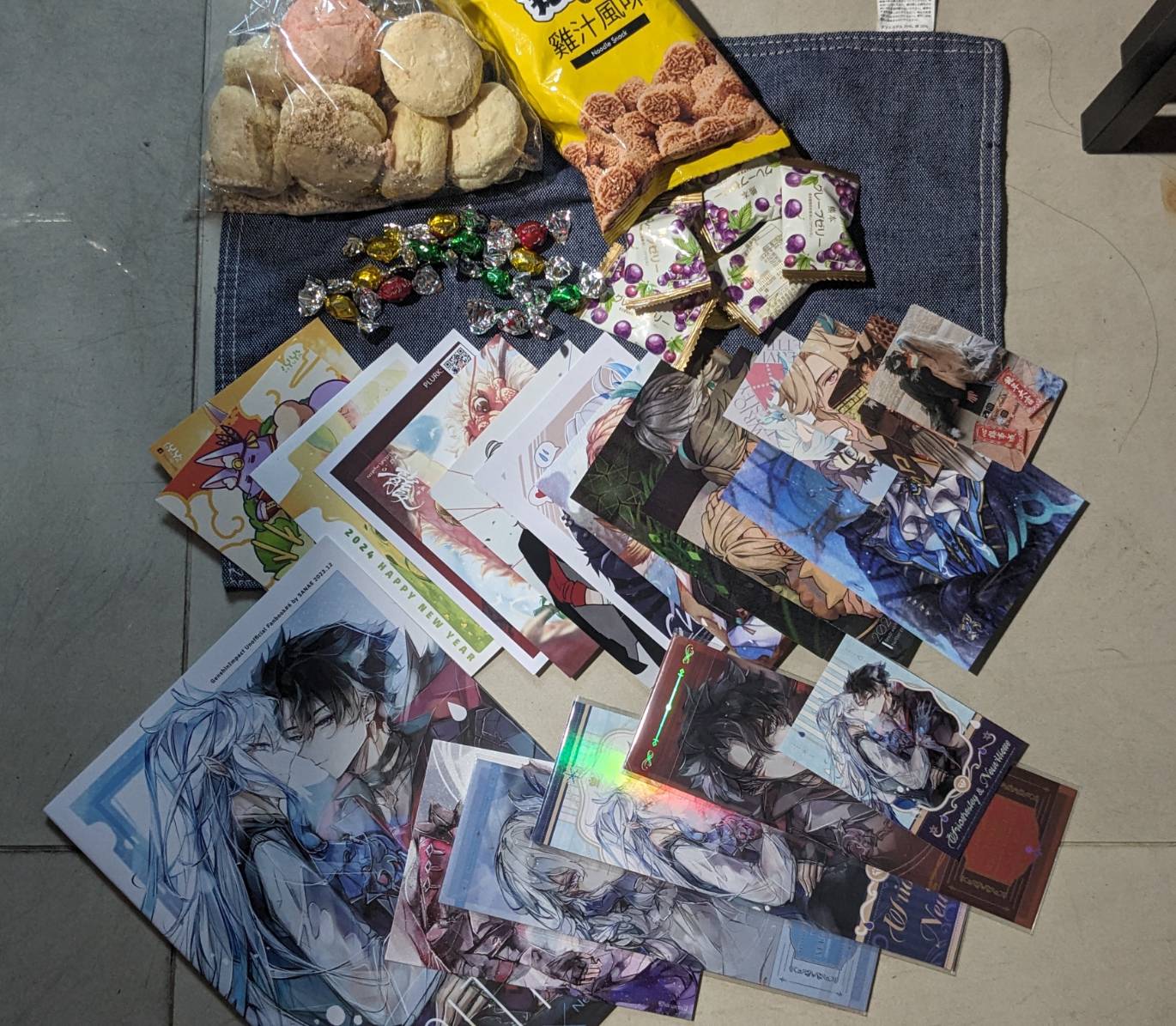 a colorful and festive scene of a collection of anime and manga books, bookmarks, snacks, and other items. there are several books with anime characters on the covers, as well as colorful bookmarks and other items. in the upper left corner, there is a bag of cookies and some candy, suggesting a gift or celebration. the overall impression is one of fun and excitement.