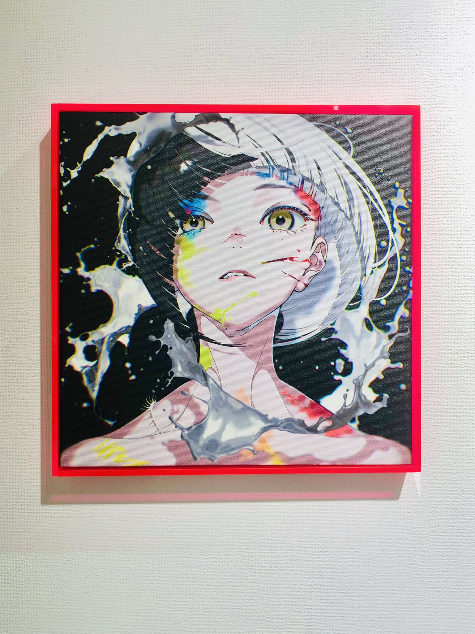 an animestyle illustration of a girl with paint splattered on her face is framed in red and hung on a white wall. the girl's hair is black on one side and white on the other, and she has streaks of color on her face. she is wearing a white shirt with a black collar. the background of the illustration is black with white paint splatters.