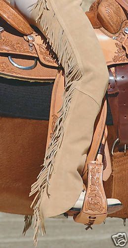 loseup view of a person wearing tan leather chaps with fringe, seated on a western saddle. the saddle is intricately carved leather, and the chaps are a light tan color. the focus is on the detail of the chaps and the saddle.