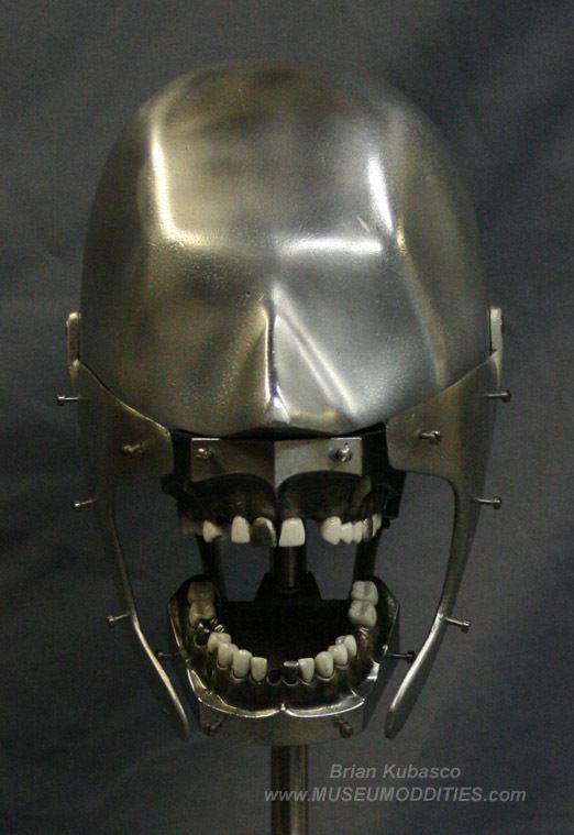 a silver colored metal dental model of a human jaw with teeth, jaw, and skull. it is sitting on a stand.