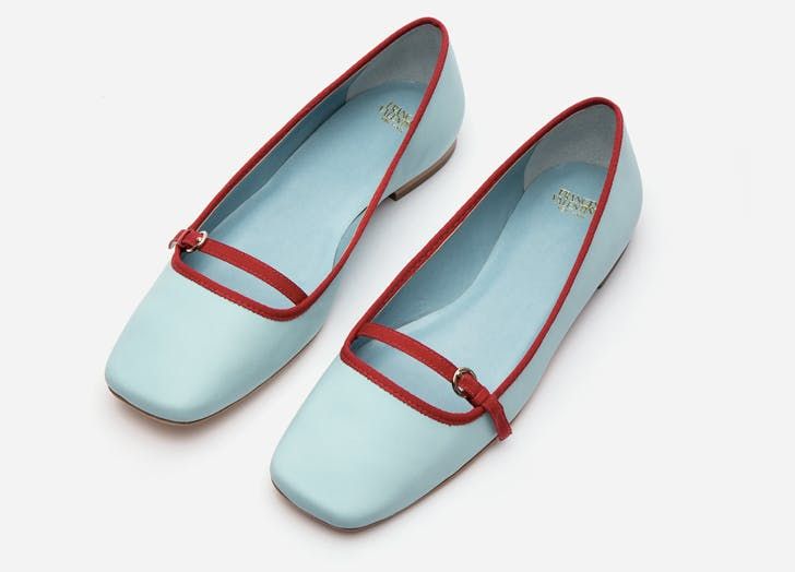 a pair of light blue ballerina flats with red trim and a strap with a buckle is displayed on a white background. the shoes are angled slightly to the right.