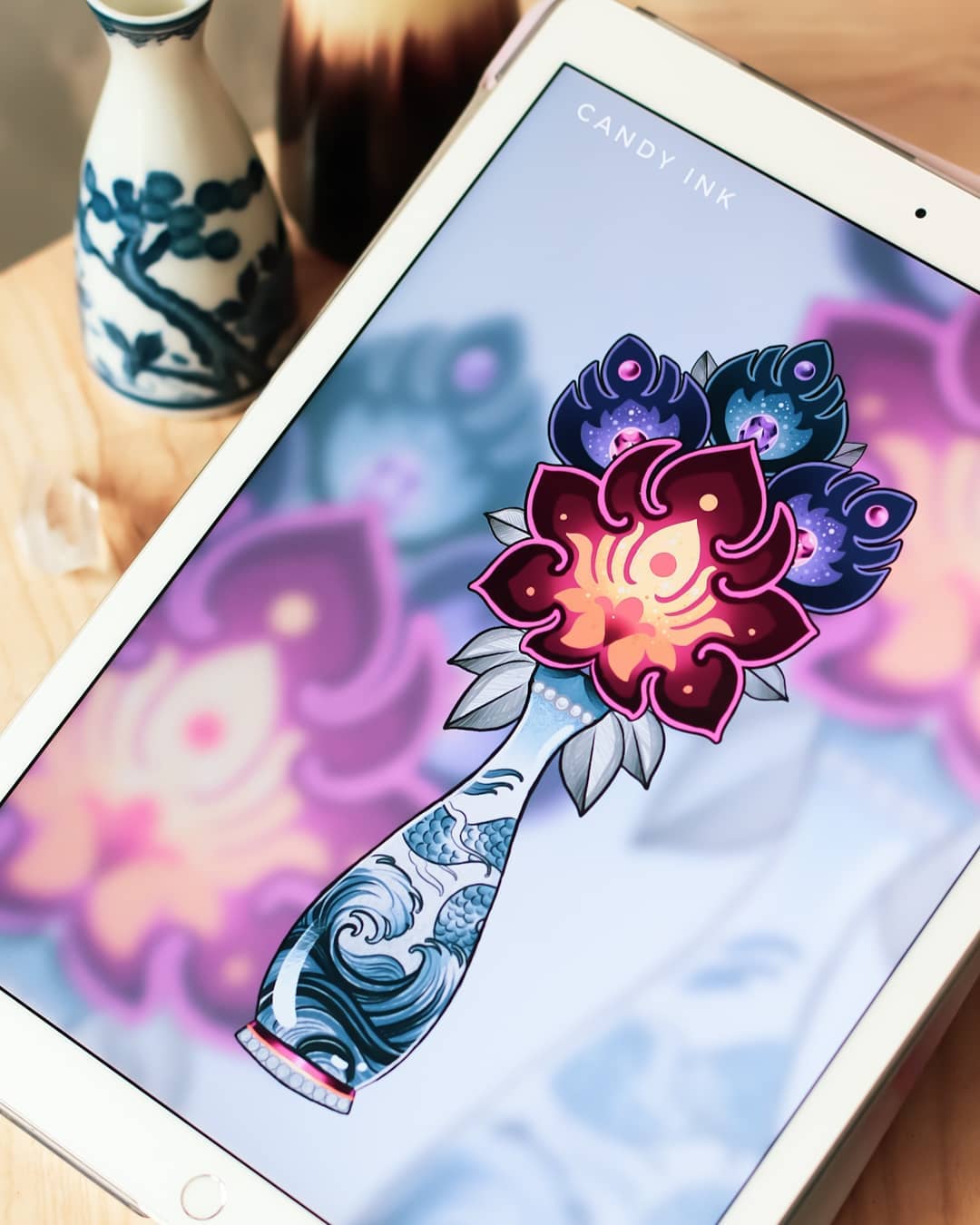 a digital illustration of a tattoo design featuring a bouquet of stylized flowers in a vase. the flowers are rendered in shades of purple, blue, and yellow, while the vase is decorated with a wave pattern. the illustration is displayed on a tablet, with a watermark reading "candy ink" in the top right corner. the background is a blurred pattern of pink and purple shapes.